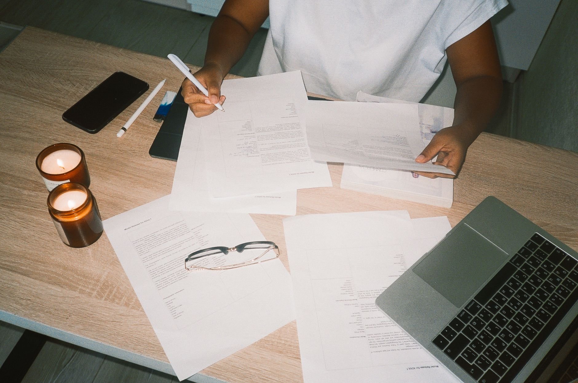 A person working at a desk with candles, documents, and a laptop, creating a cozy office atmosphere.